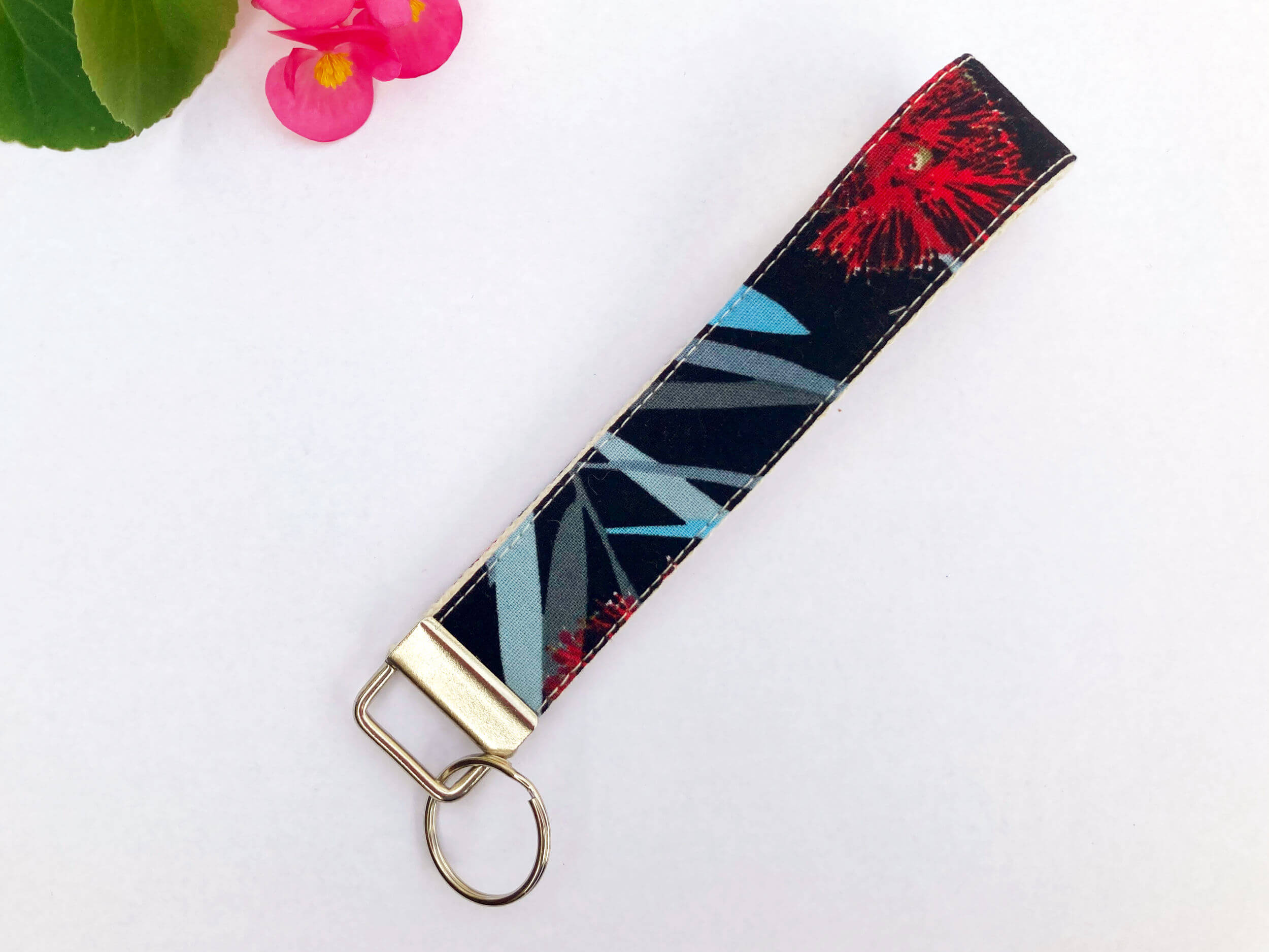 Key fob with a print that has a black background, red bottlebrush, and parts of blue and grey leaves. Background is white.