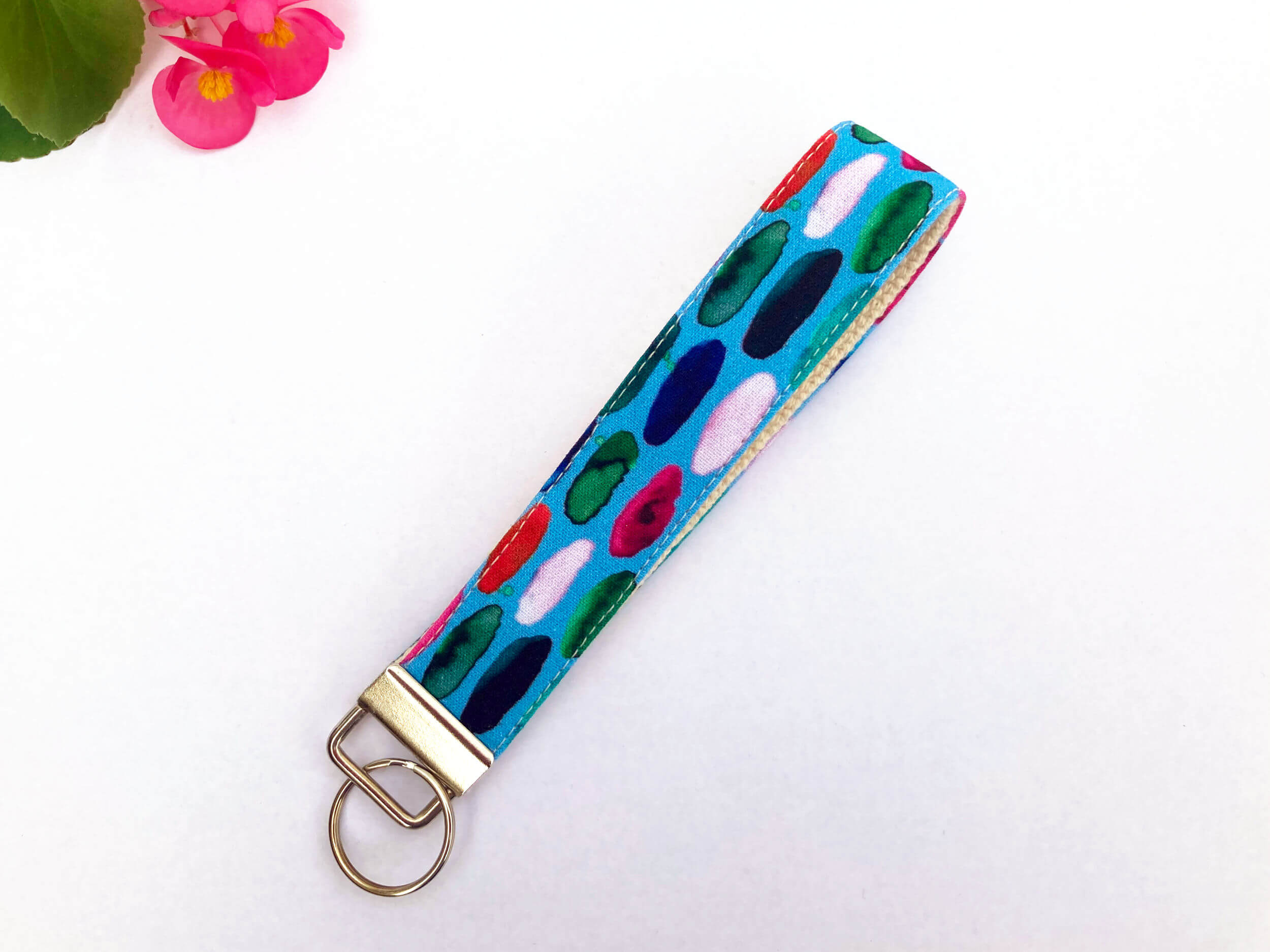 Key fob laying at an angle with multicoloured finger painted dashes on a blue background. Nickel hardware. Background is white.