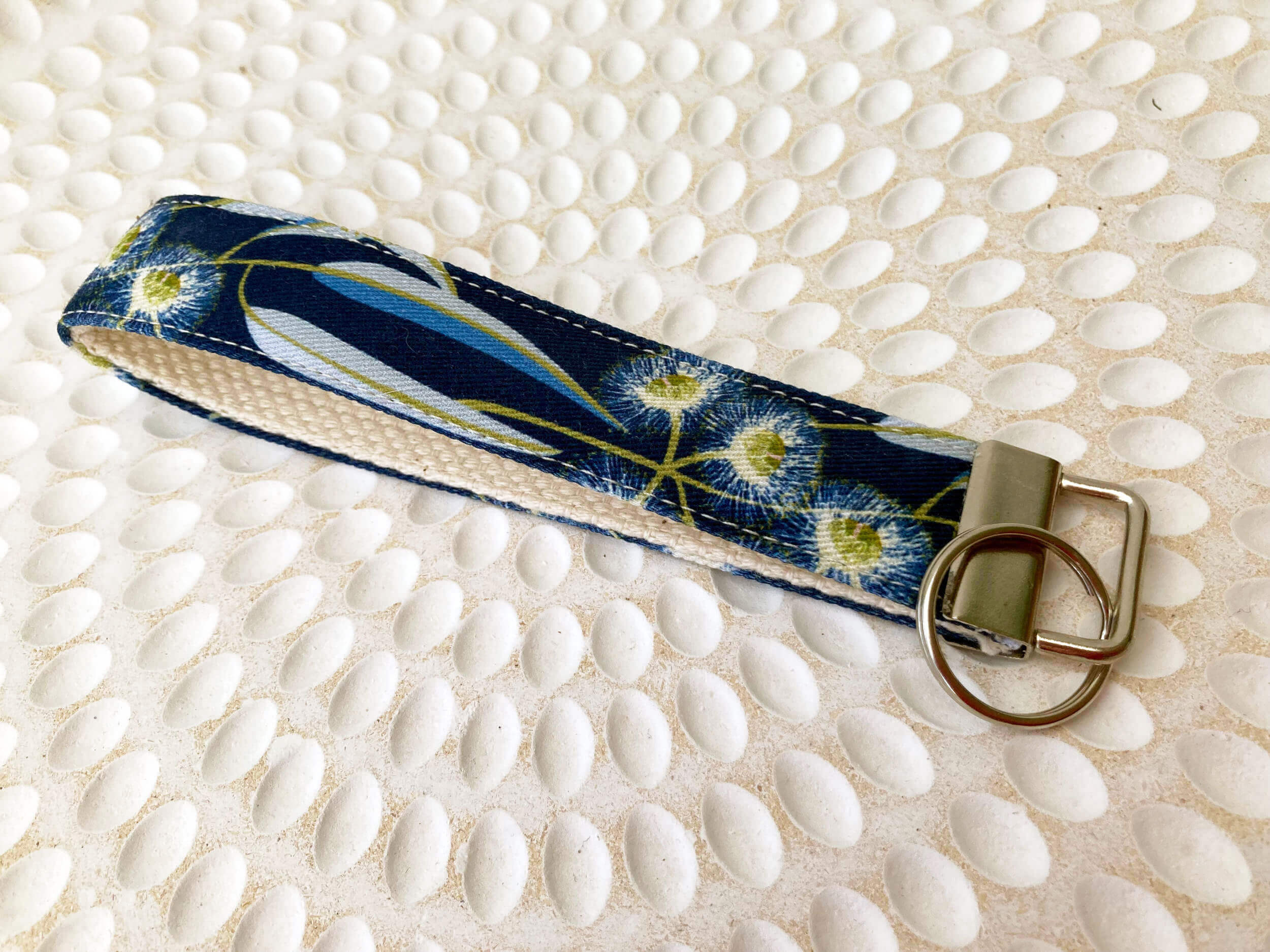 Key fob with navy background with gum leaves. Laying on white textured plate background.