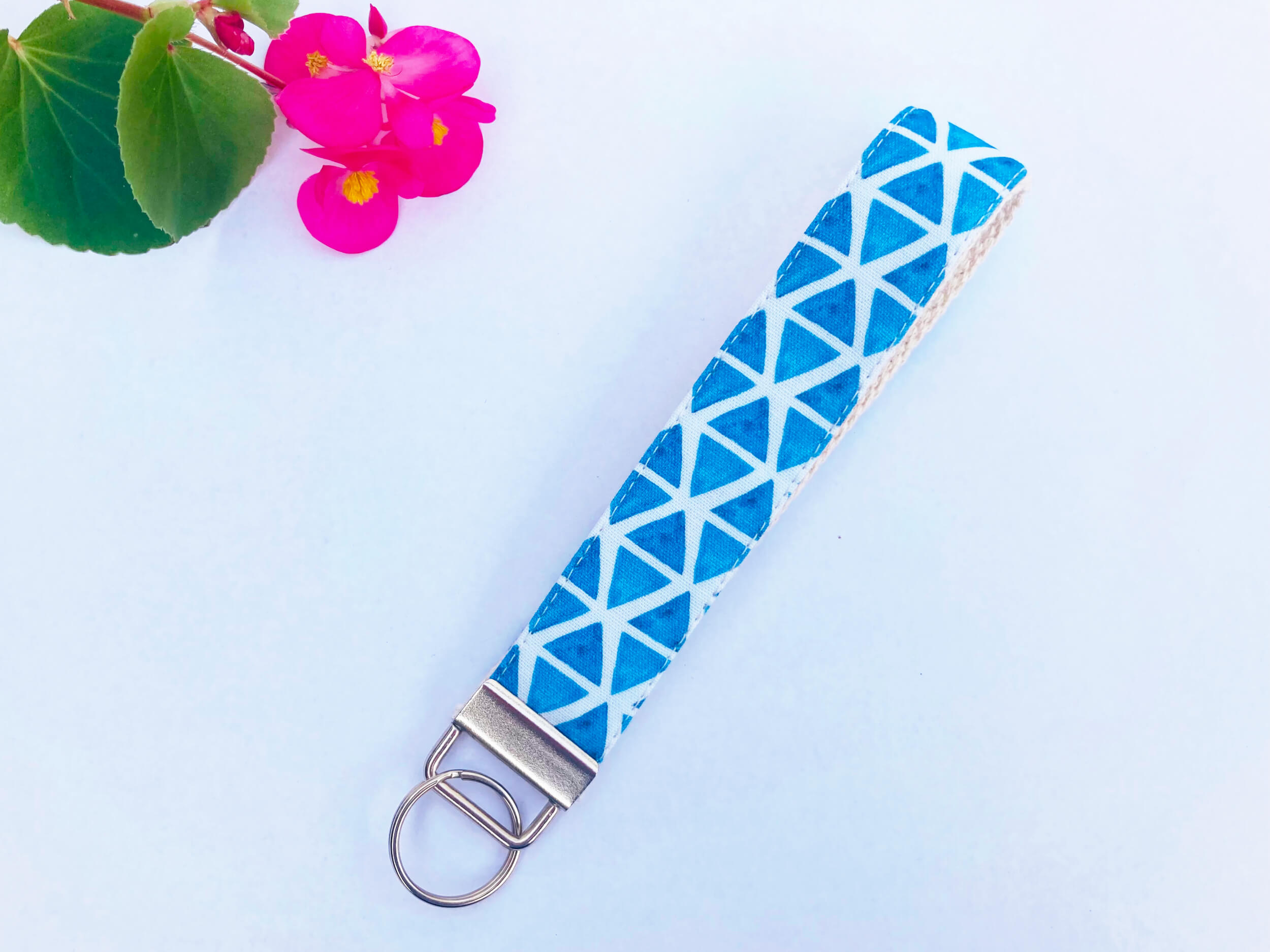 Key fob with light blue triangles on a white background print. Background is white and a pink flower and leaves are in the corner.