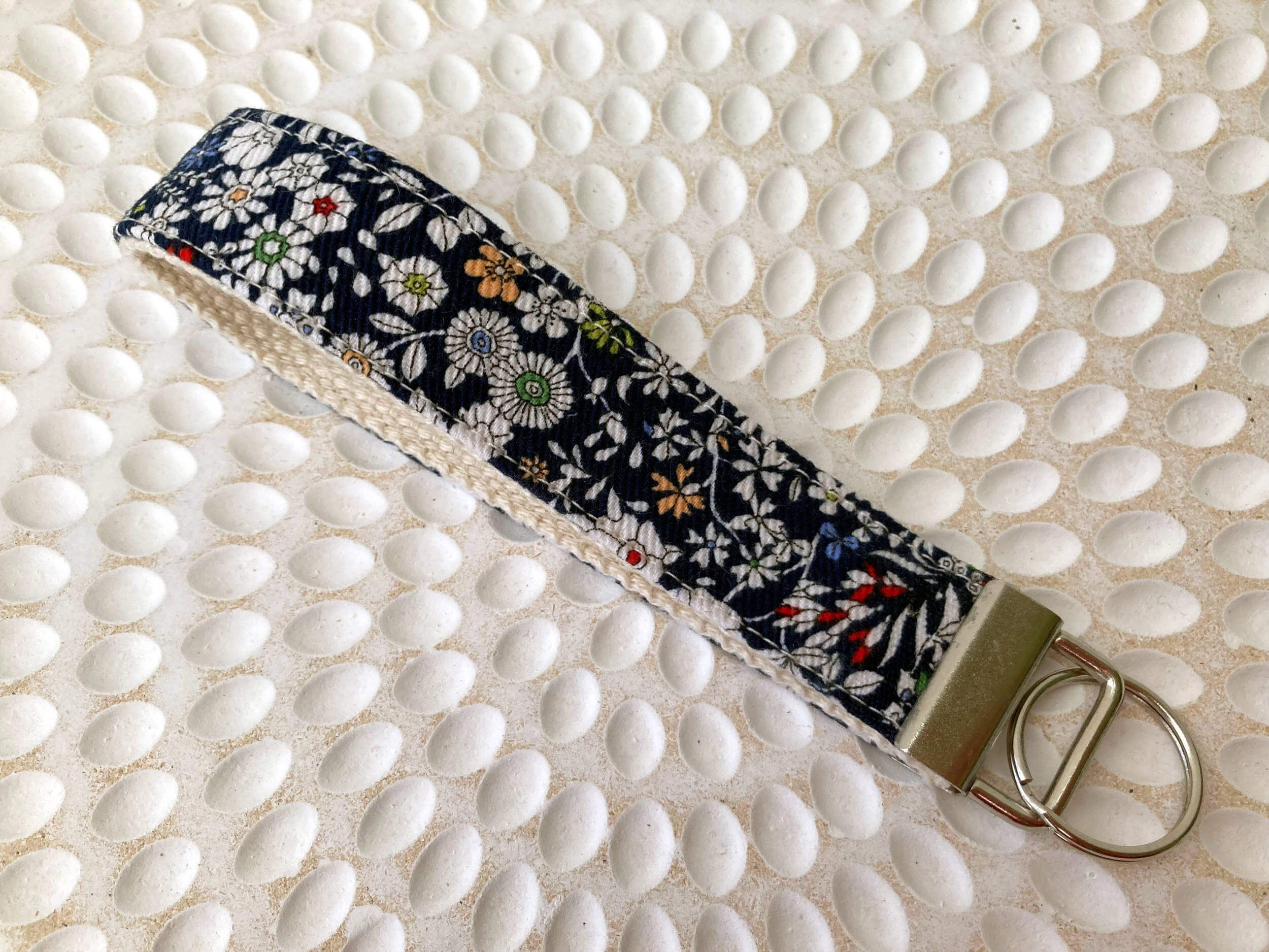 Key fob with white flowers and navy background on a white textured surface