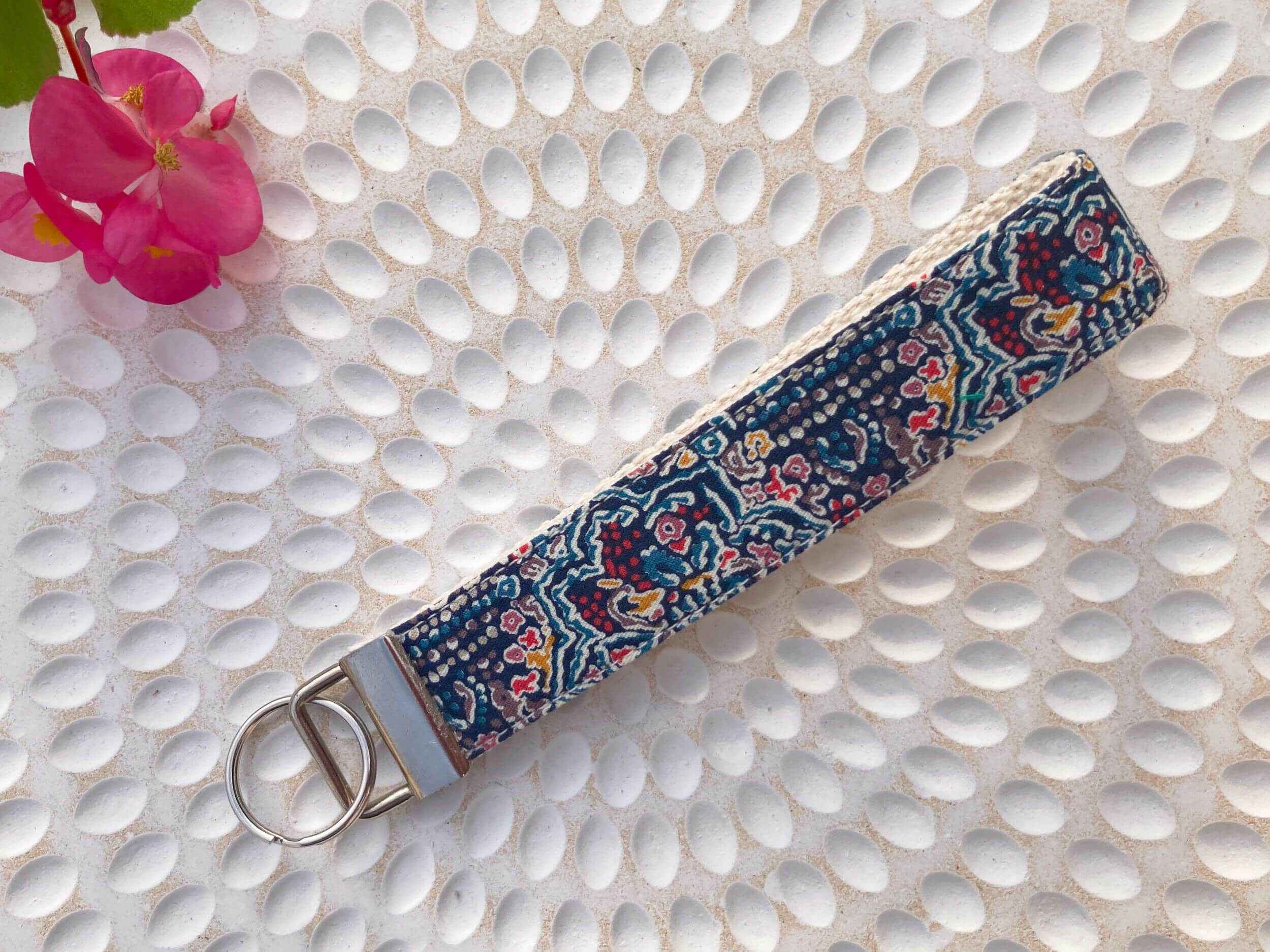 Key fob in a Liberty of London print called Ruby Templar on a textured background with a pink flower in the corner.