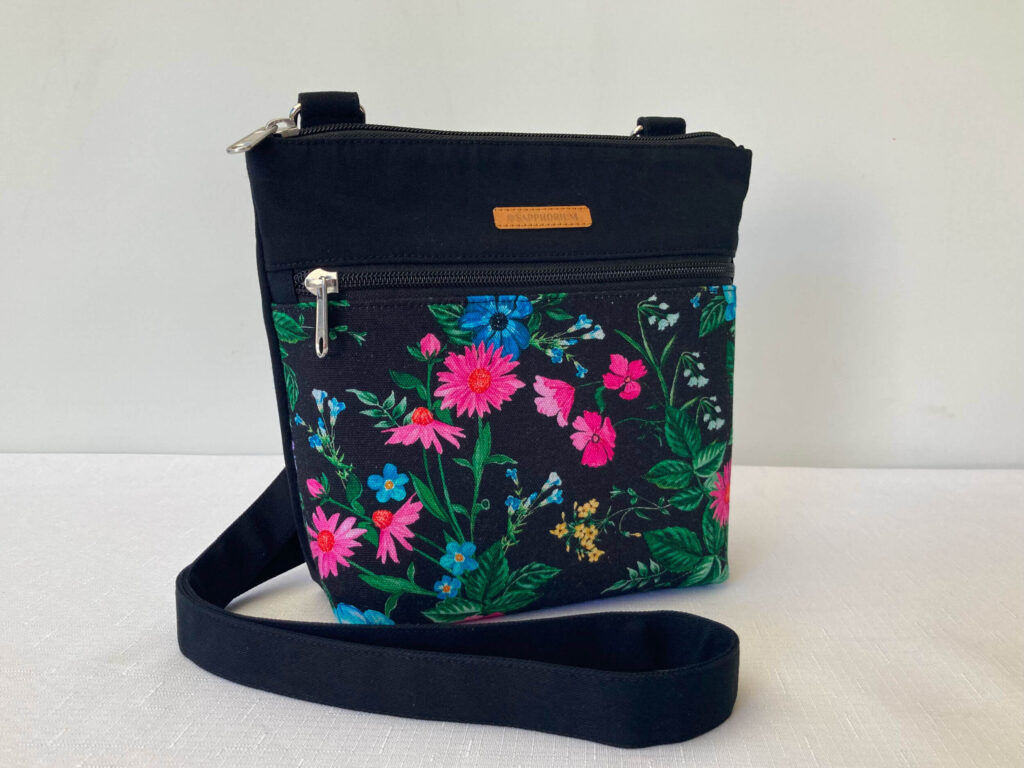 Black Crossbody bag with a floral print on a white tablecloth and white background.