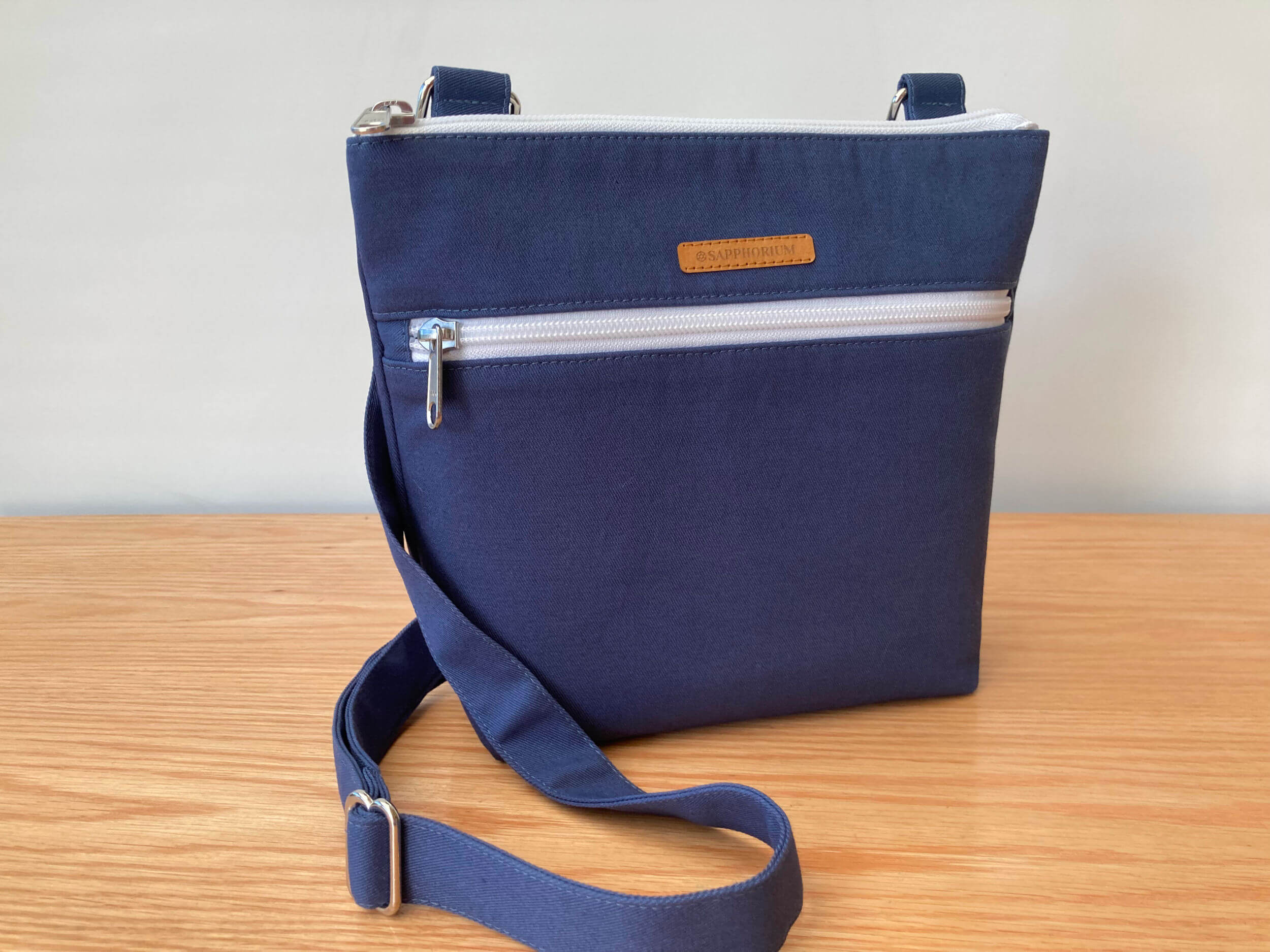 Marine Blue Crossbody Bag with 2 white zips on a wooden table and white background.