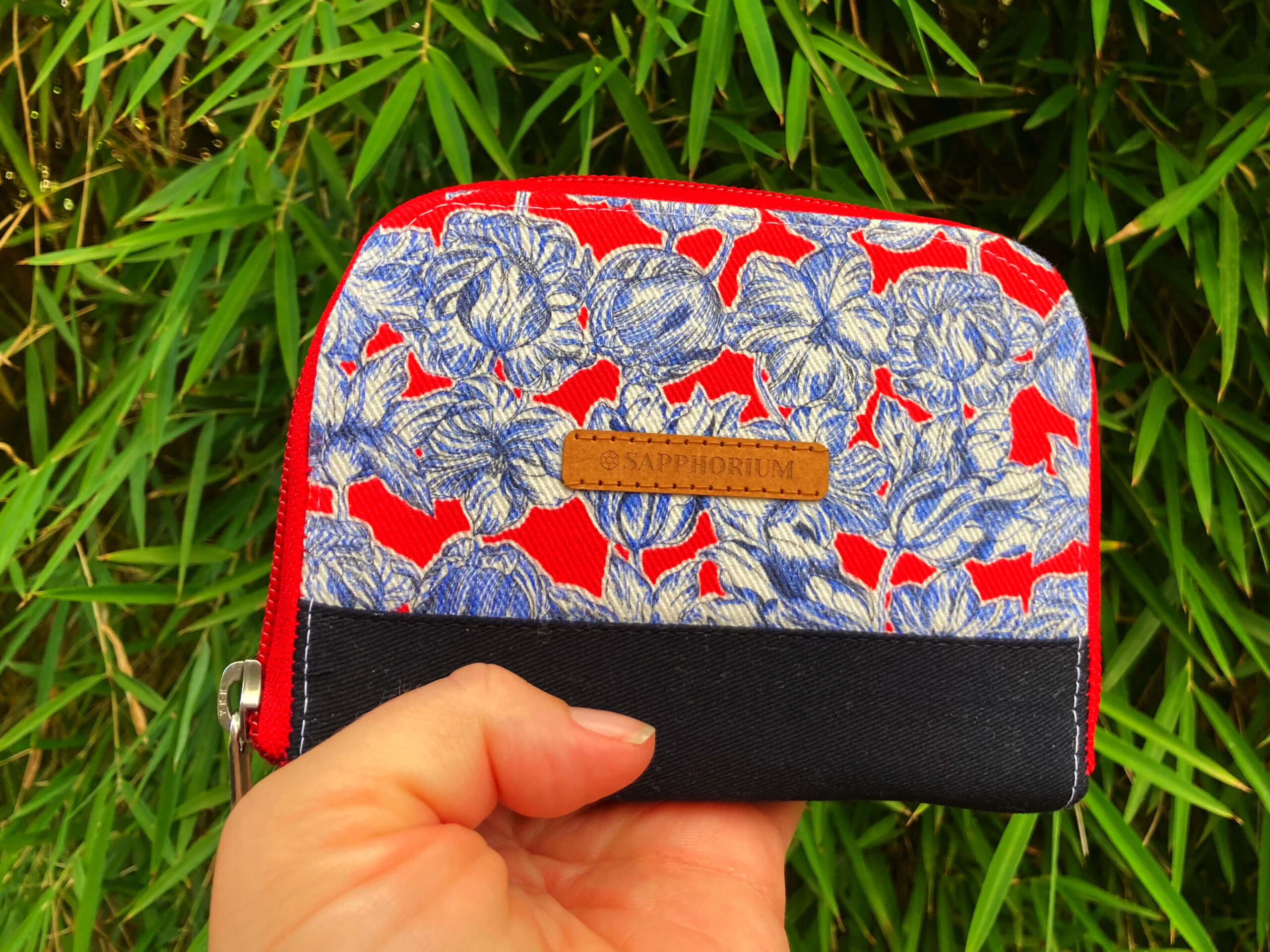 Fabric wallet with red zip, blue white and red floral print and navy accent. Brown label reads Sapphorium.