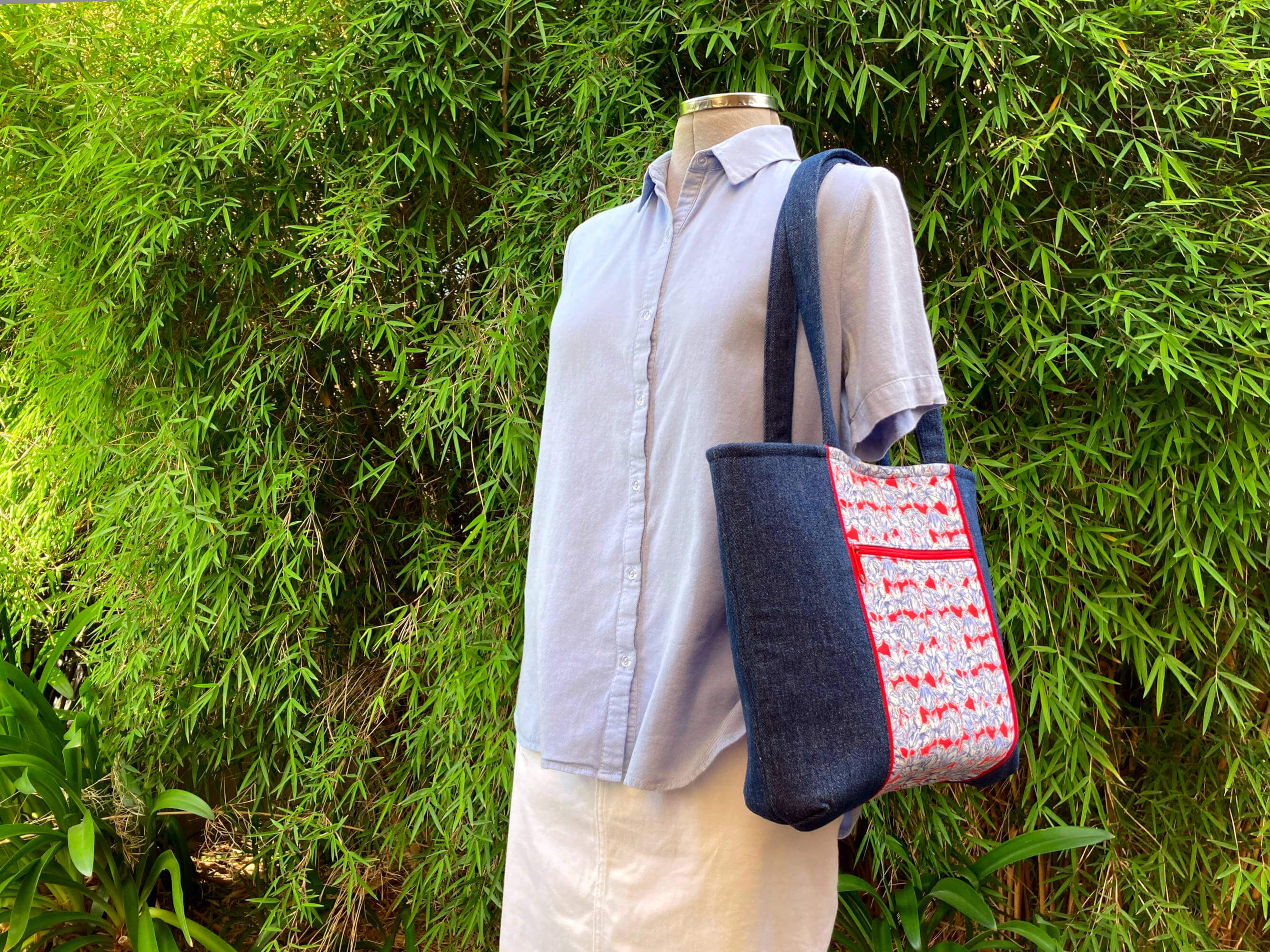 Mannequin wearing light blue shirt and white skirt with tote bag on shoulder and leafy green background