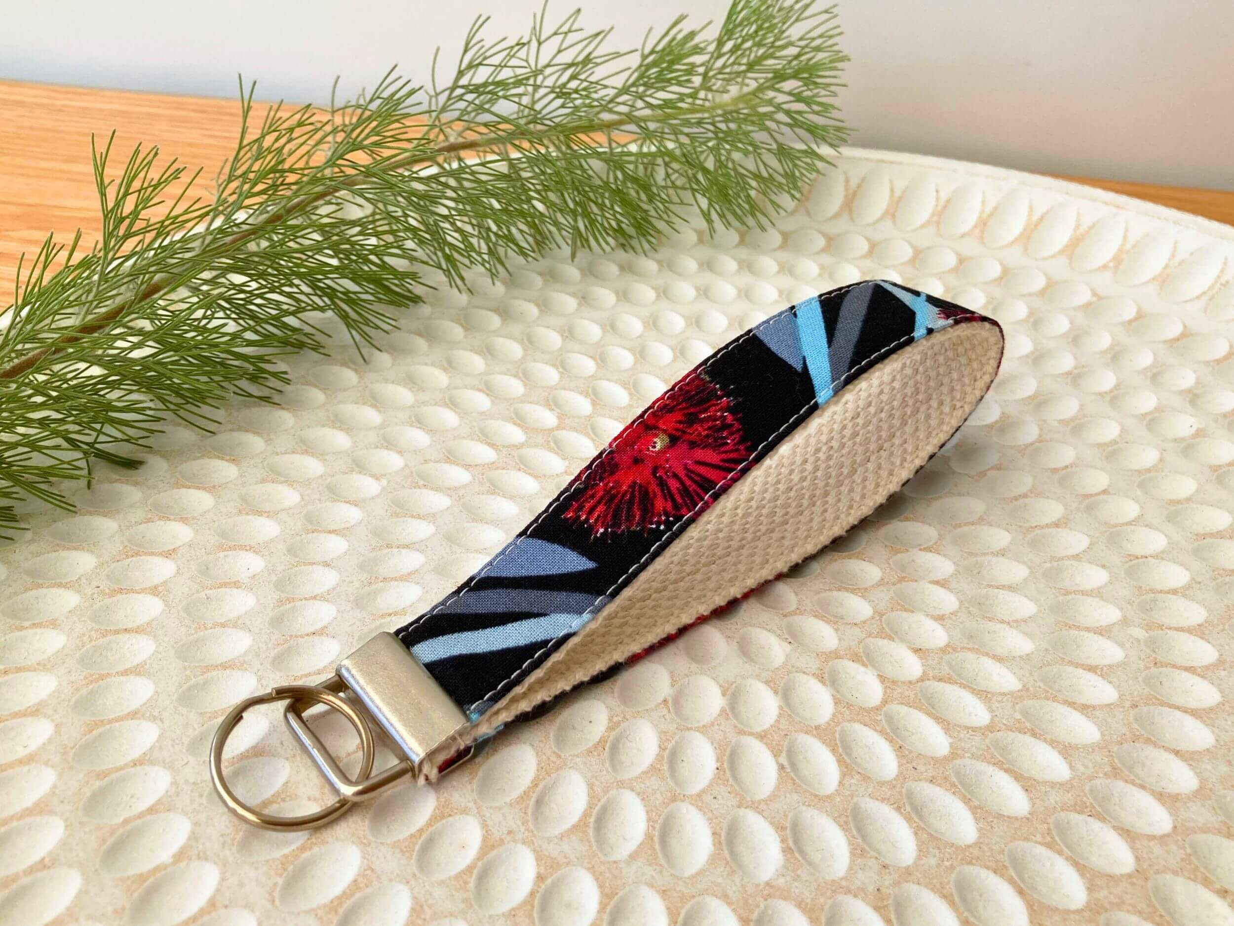 Key fob in a black and red bottlebrush print, on a textured white plate with fine leaved plant cutting in top left corner. Handmade by Sapphorium.