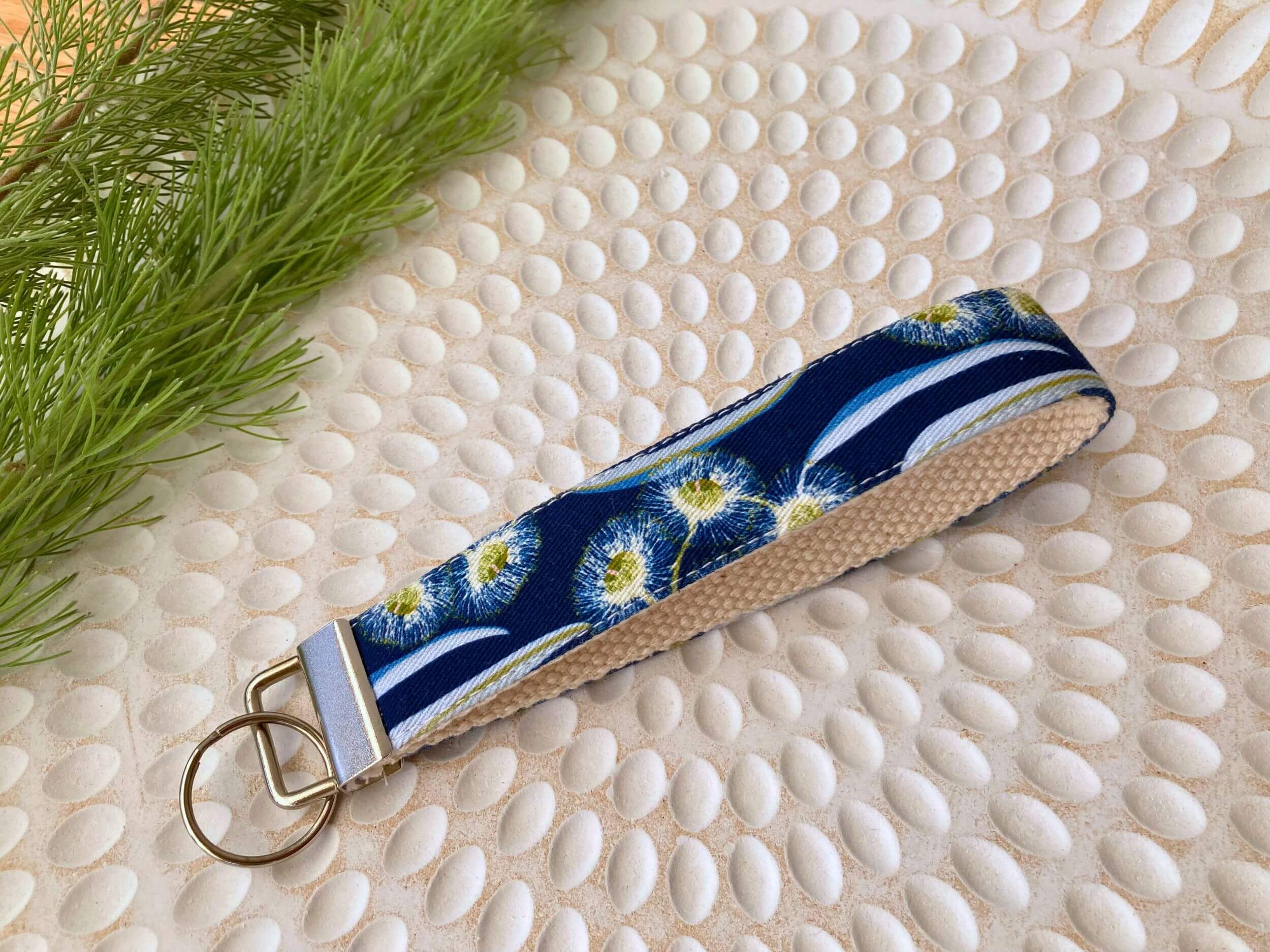Key fob in a blue gums print, on a textured white plate with fine leaved plant cutting in top left corner. Handmade by Sapphorium.