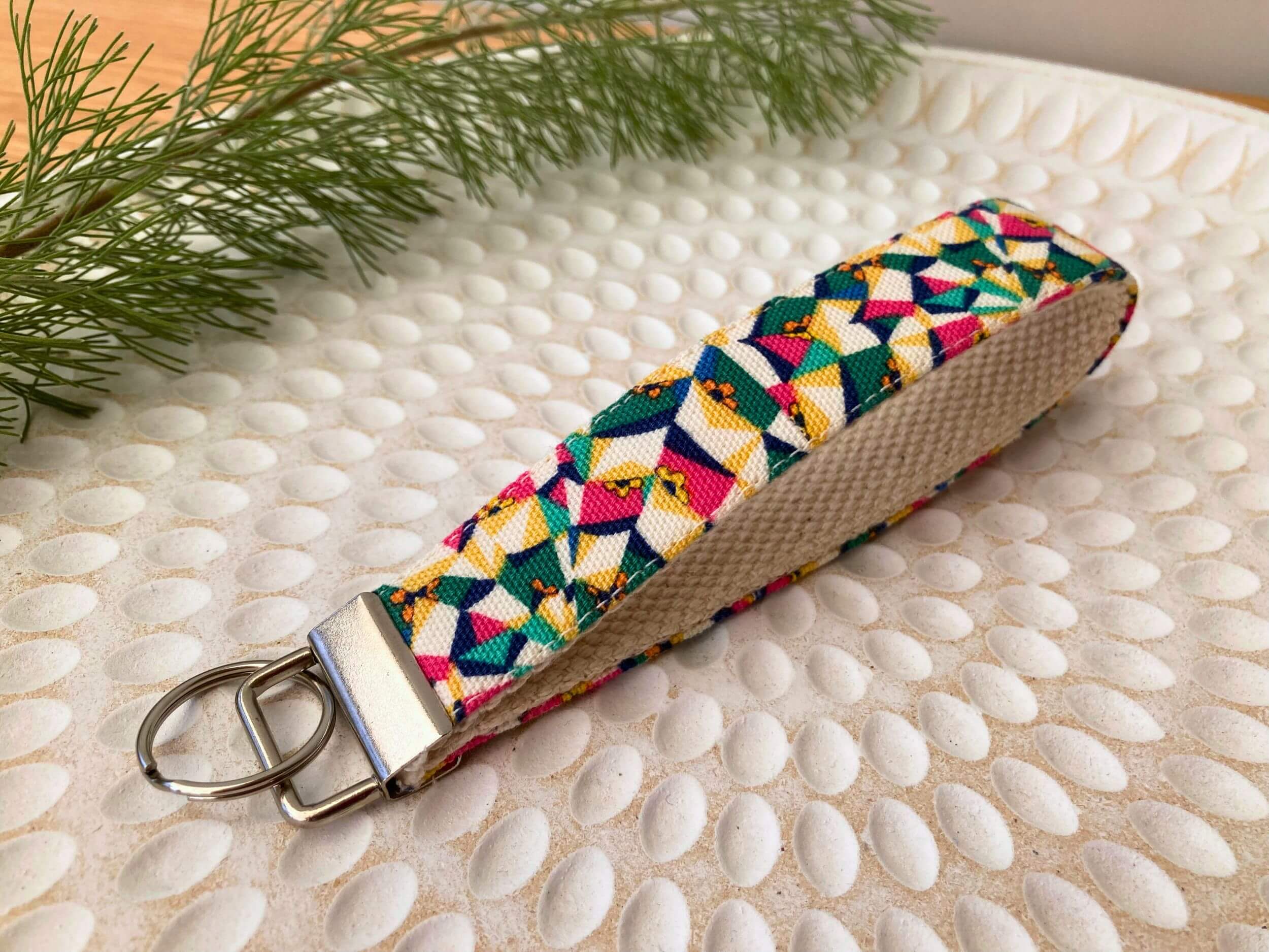 Key fob in a Liberty Poppy's Patchwork Yellow print, on a textured white plate with fine leaved plant cutting in top left corner. Handmade by Sapphorium.