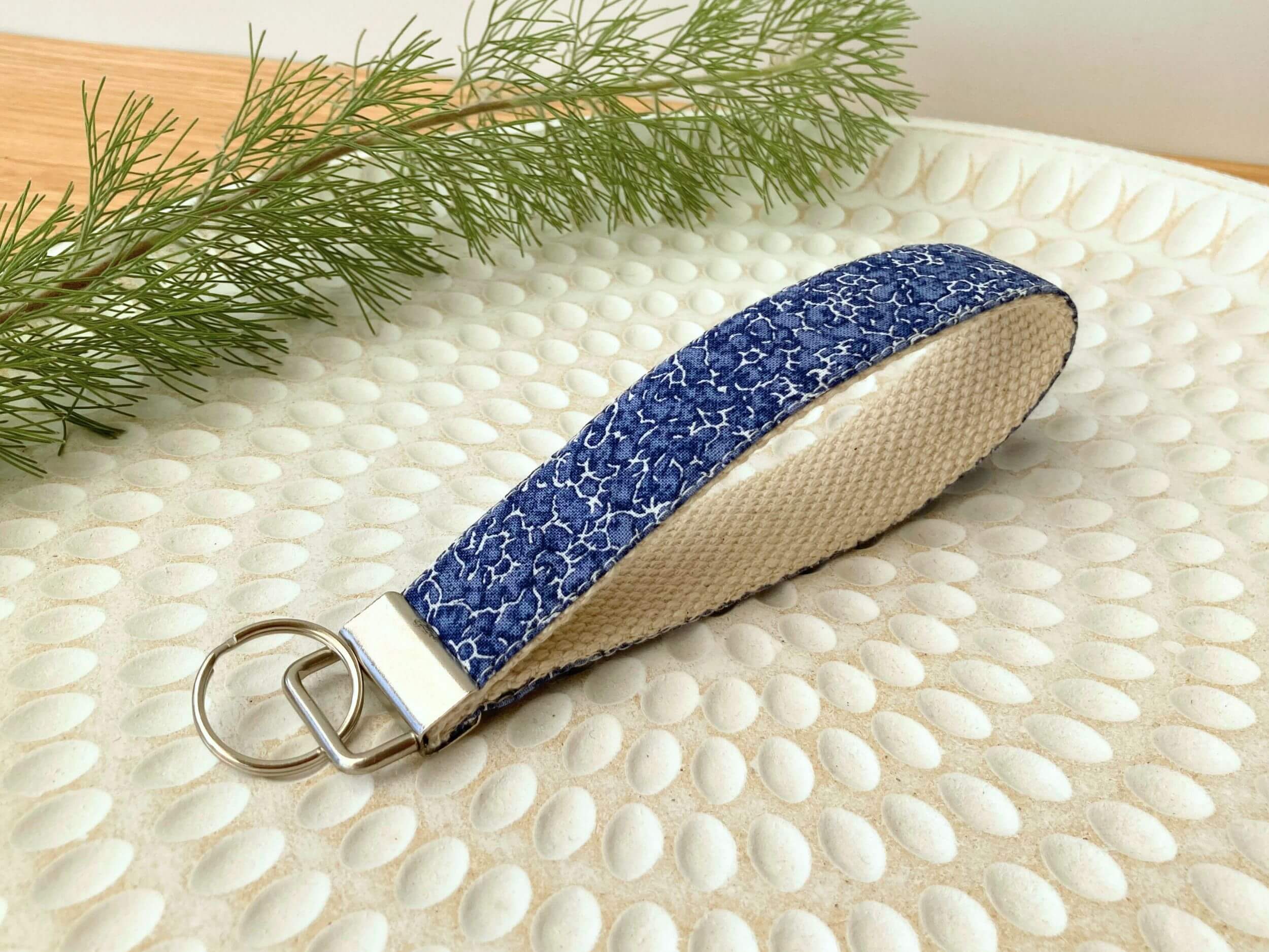 Key fob in a navy crackle print, on a textured white plate with fine leaved plant cutting in top left corner. Handmade by Sapphorium.