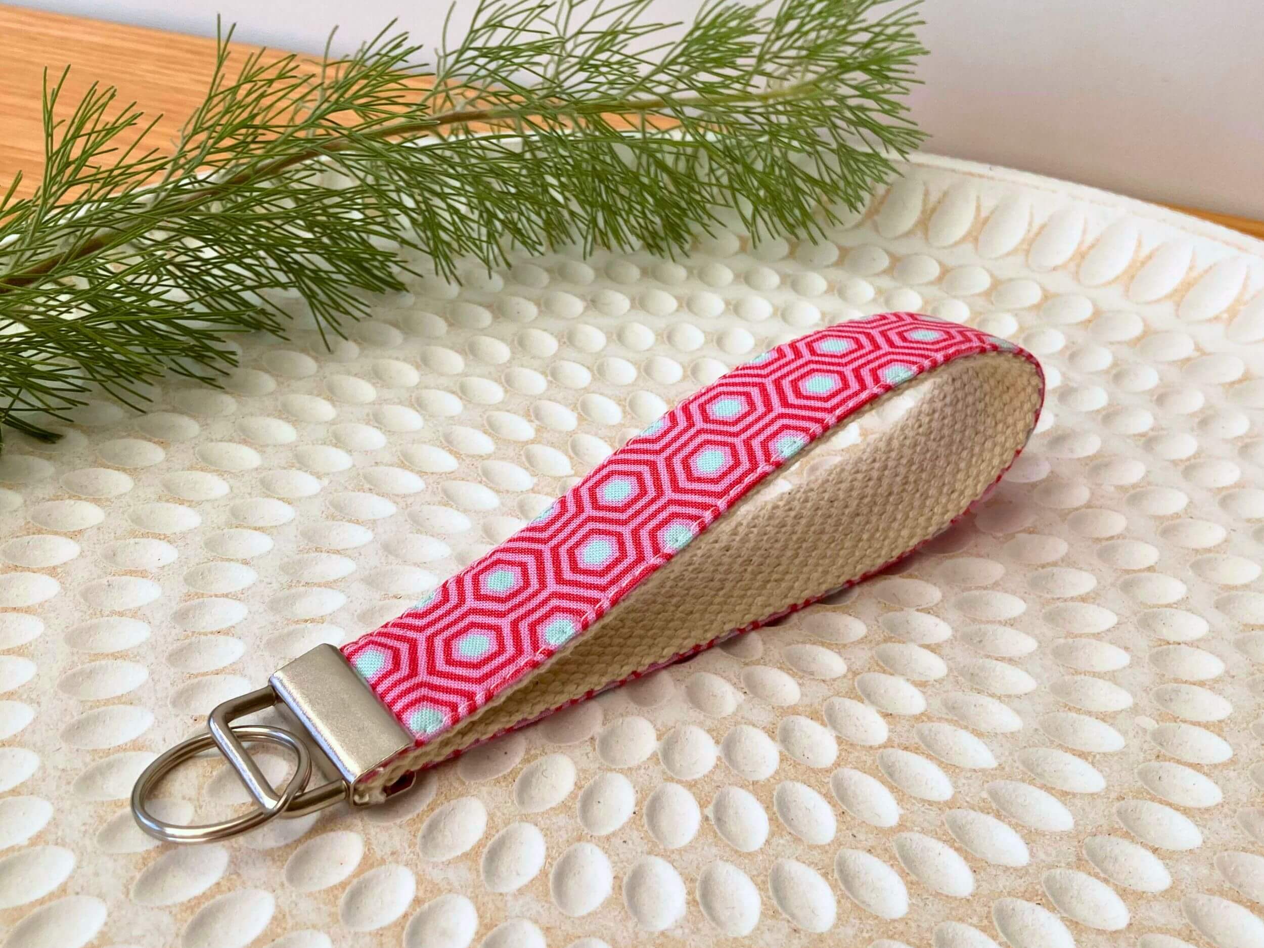 Key fob in a pink hexagon print, on a textured white plate with fine leaved plant cutting in top left corner. Handmade by Sapphorium.