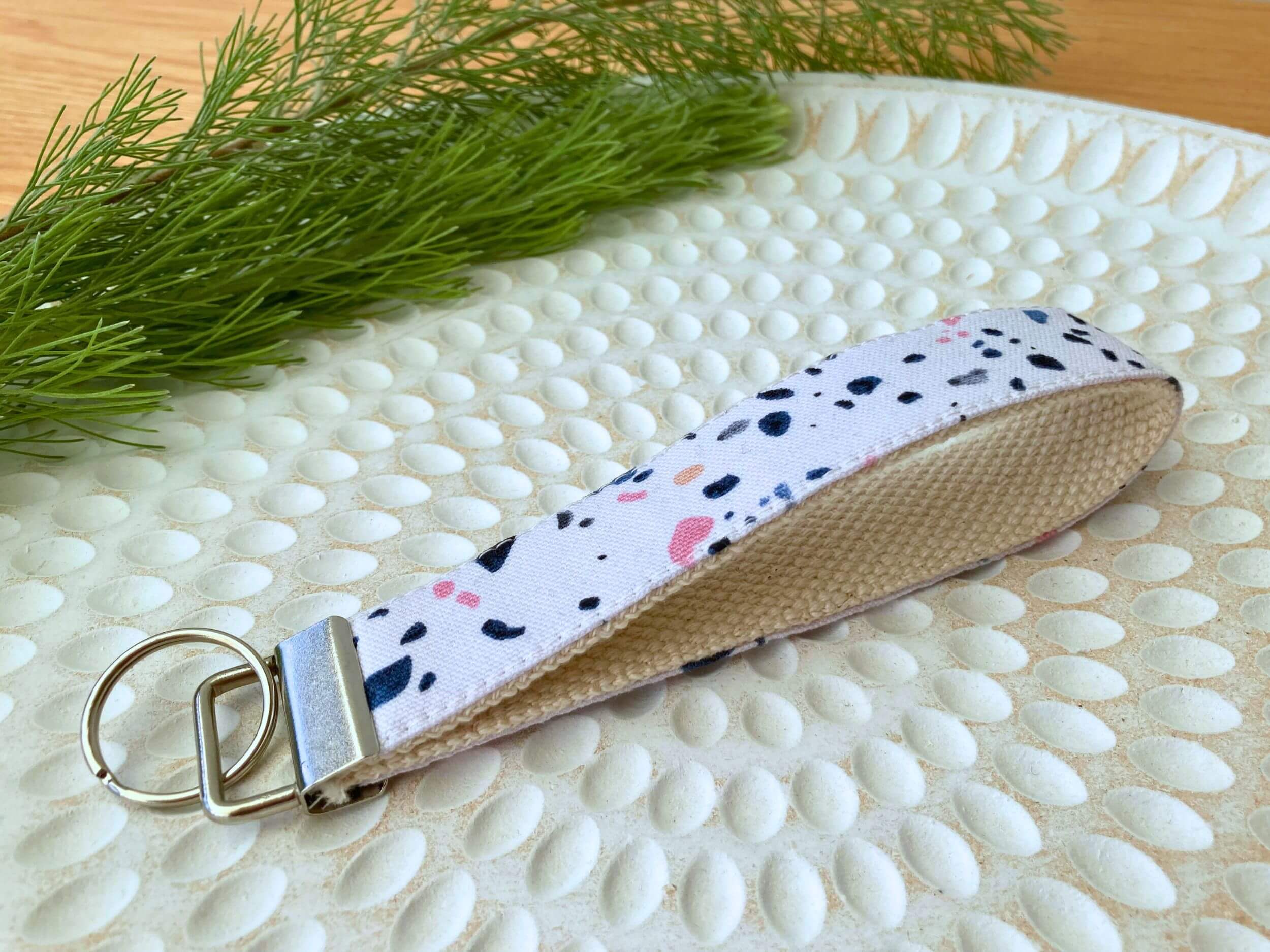 Key fob in a white with pink and blue marble print, on a textured white plate with fine leaved plant cutting in top left corner. Handmade by Sapphorium.